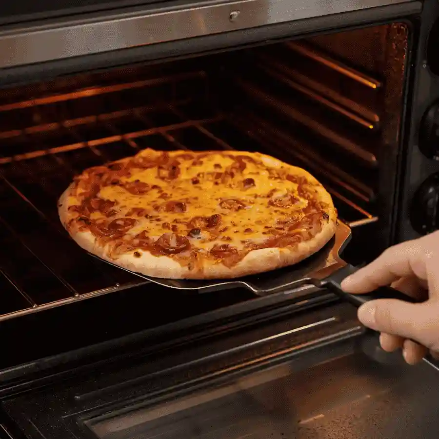 Personal frozen pizza being removed from a toaster oven with melted cheese